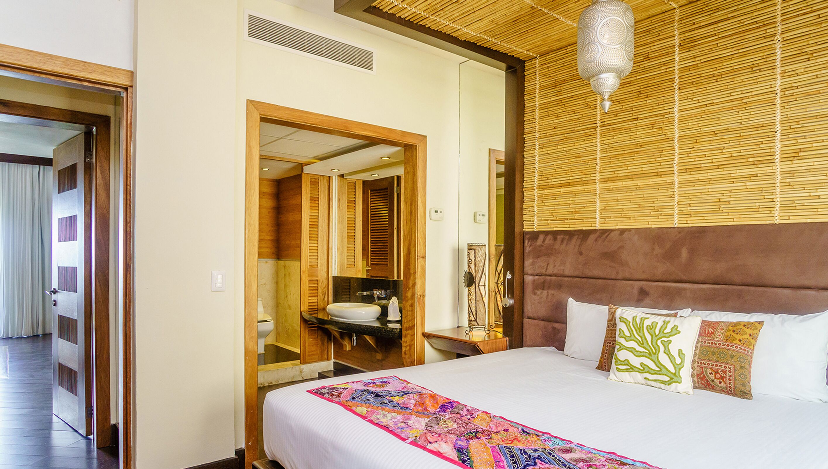A hotel room with a large bed, a wooden headboard, a mirror, and a ceiling fan.