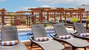 Un área de piscina en la azotea con sillones de descanso y una pérgola de madera.