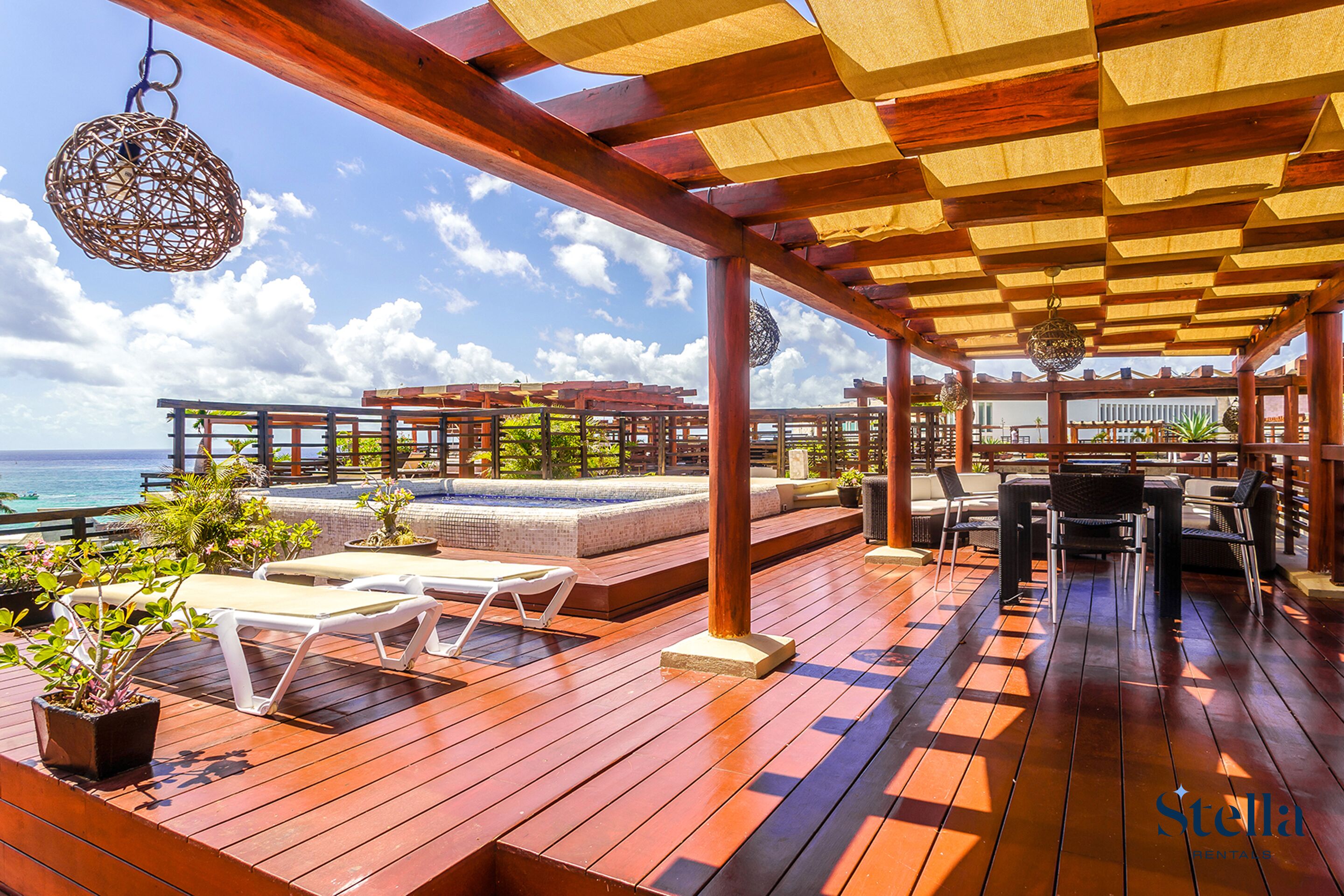 A wooden deck with lounge chairs, a hot tub, and a view of the ocean.