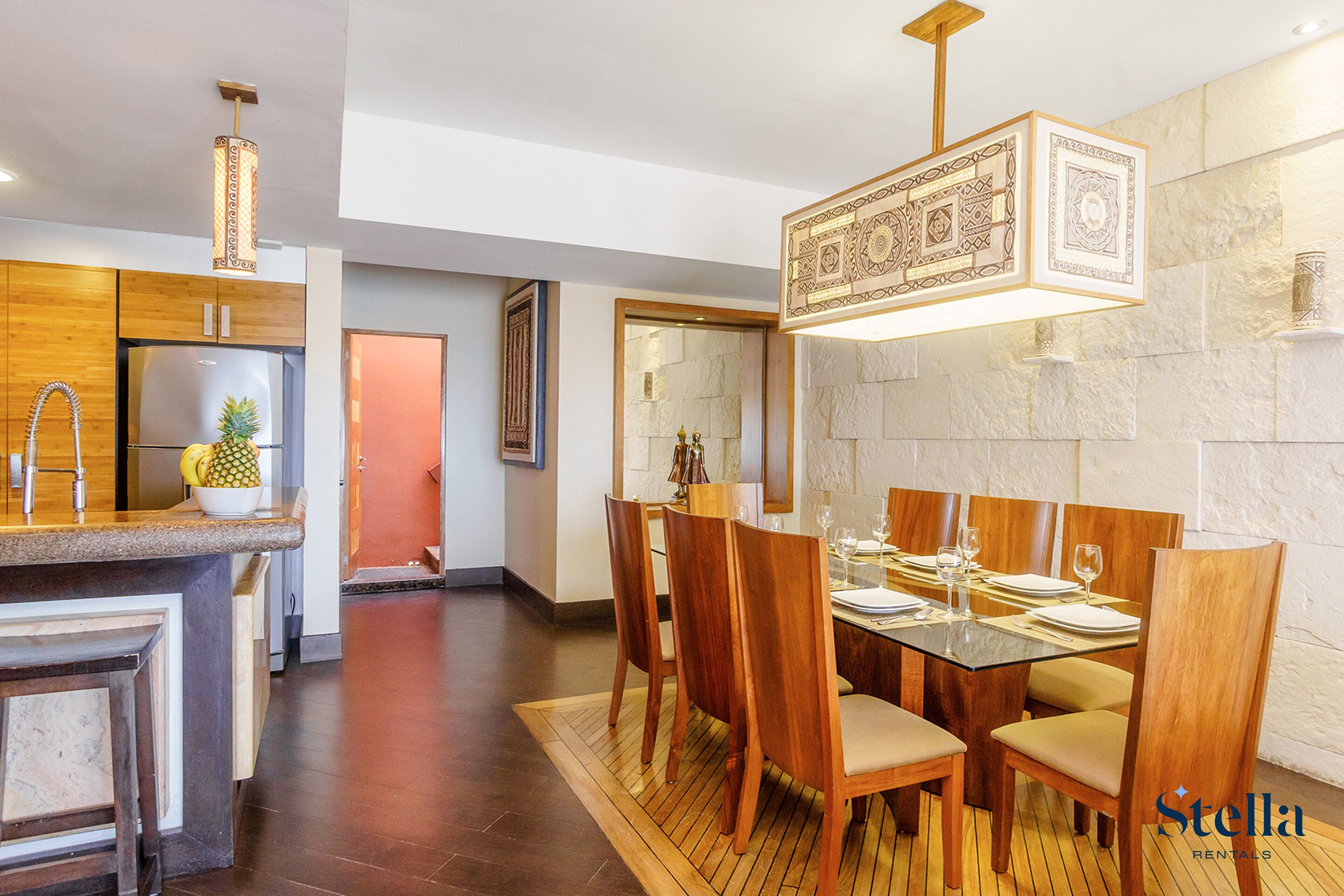 A modern kitchen with wooden cabinets, a stainless steel refrigerator, and a dining area with wooden chairs and a glass table.