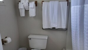 A bathroom with a toilet, a small trash bin, a towel rack with several towels, and a shower curtain. - Sandman Motel (Libby)
