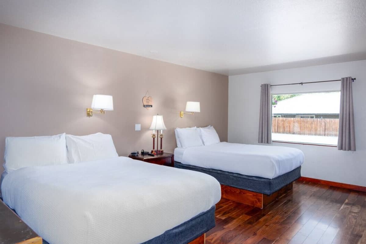 Une chambre d’hôtel avec deux lits, un plancher en bois et une fenêtre avec des rideaux.