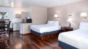 A hotel room with two beds, a desk with a microwave, a chair, and a small kitchenette. - Sandman Motel (Libby)