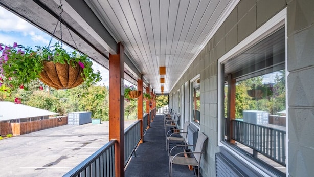 A covered outdoor area with chairs and hanging flower baskets. - Sandman Motel (Libby)