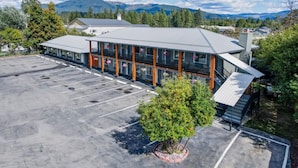 A hotel with a large parking lot, a covered outdoor area, and a view of mountains in the background. - Sandman Motel (Libby)