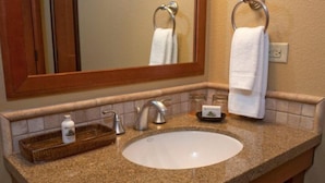 A bathroom with a granite countertop, a white sink, a mirror, and two towel rings.