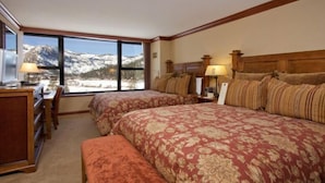 A hotel room with two beds, a desk, and a view of snow-capped mountains.