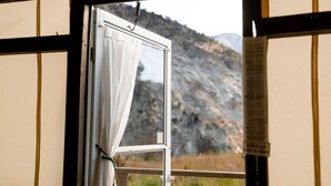 Una ventana con cortina, vista de un paisaje montañoso y un cartel en el marco.