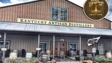 Het gebouw van Kentucky Artisan Distillery met een rustieke buitenkant, houten vaten en een bord voor bezoekersparkeren.