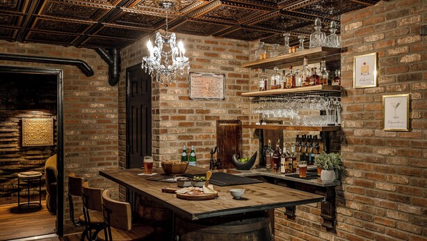 Un coin bar au style rustique, avec un comptoir en bois, des tabourets et une variété de bouteilles et de verres.