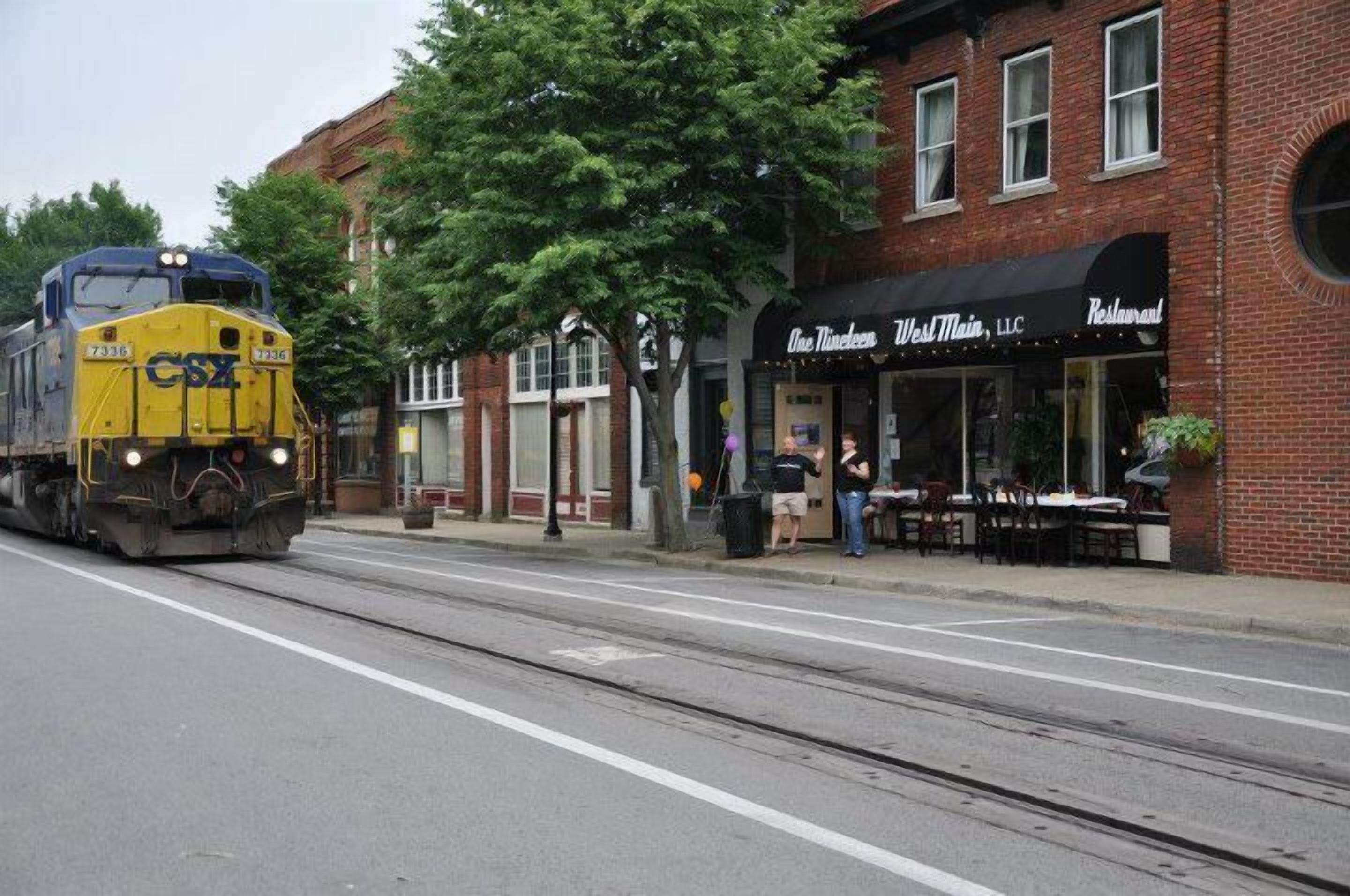 Un tren de CSX pasa cerca de un edificio de ladrillo con un restaurante llamado 'One Nineteen West Main, LLC'.