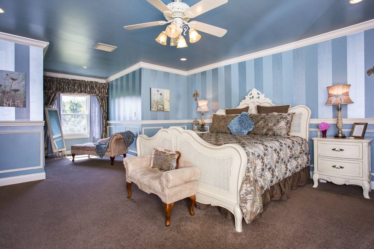 A bedroom with a large bed, a chair, a nightstand, and a ceiling fan.