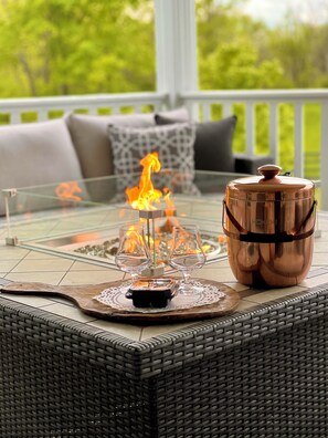 A glass-top table with a fire feature, a copper pot, and a woven chair on a patio. - Pillow and Paddock B&B (La Grange)