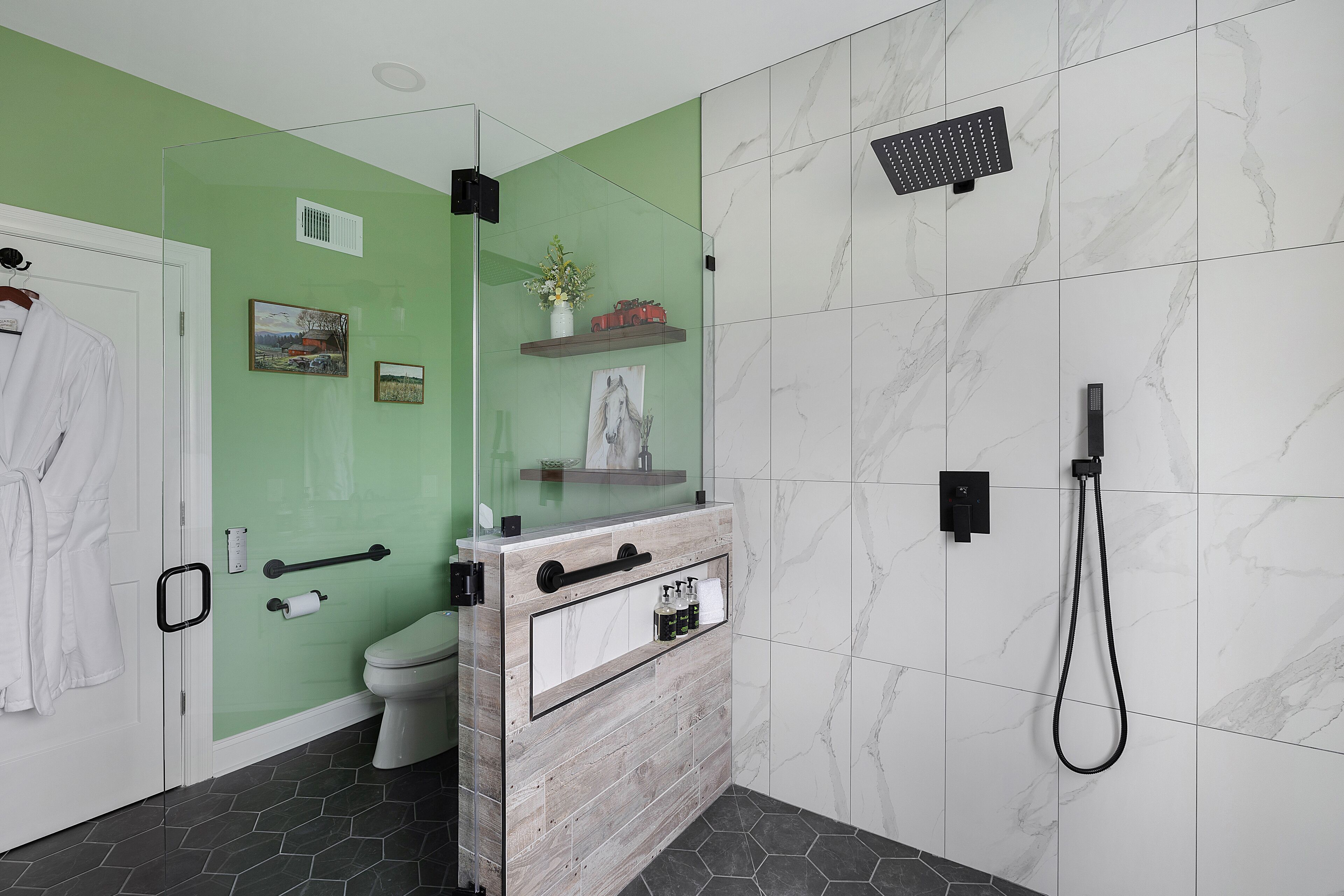 A bathroom with a green wall, a white toilet, a shower area with a handheld showerhead, and a wooden vanity with a mirror.
