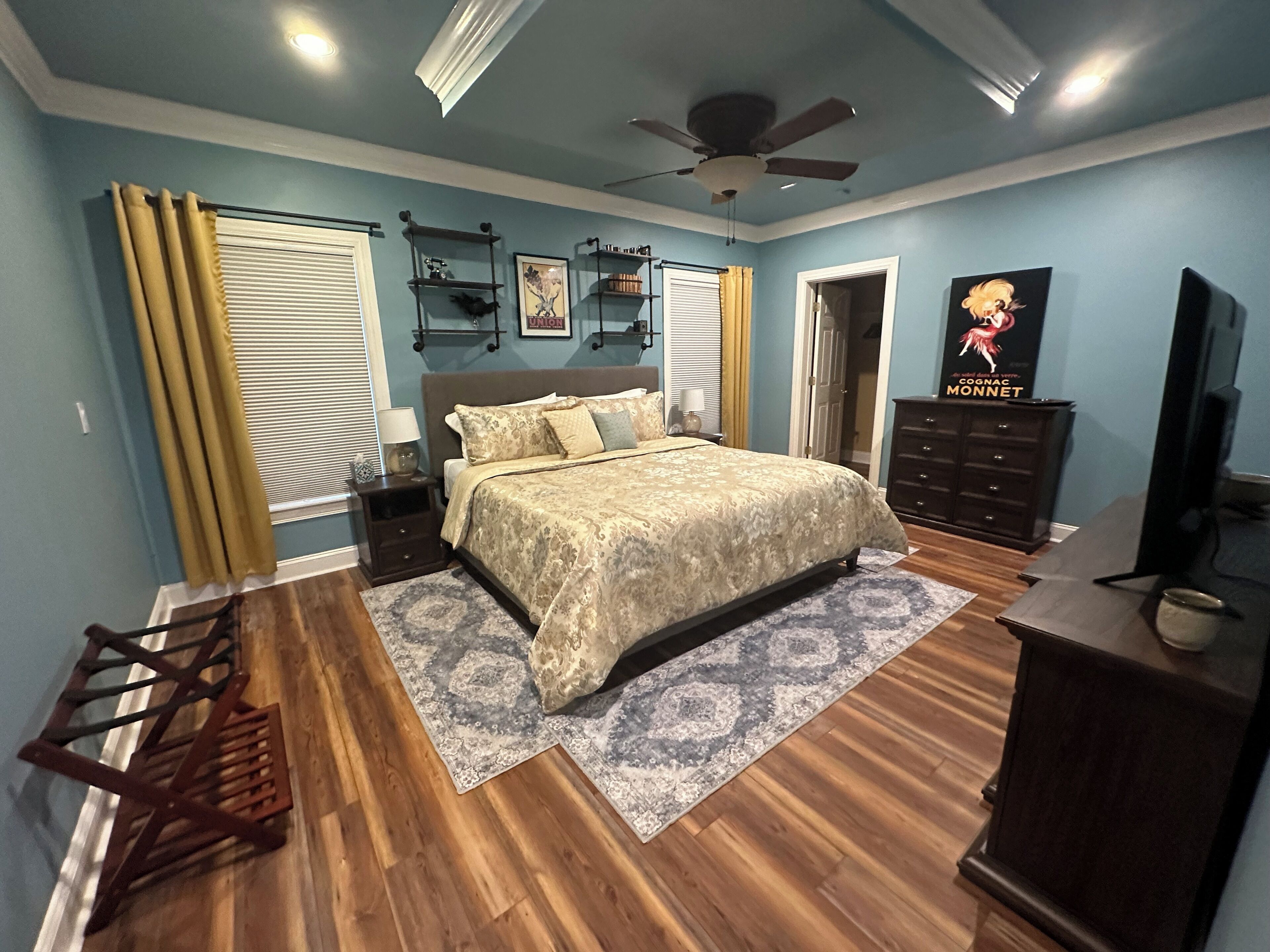 A bedroom with a bed, wooden floor, ceiling fan, and a TV.