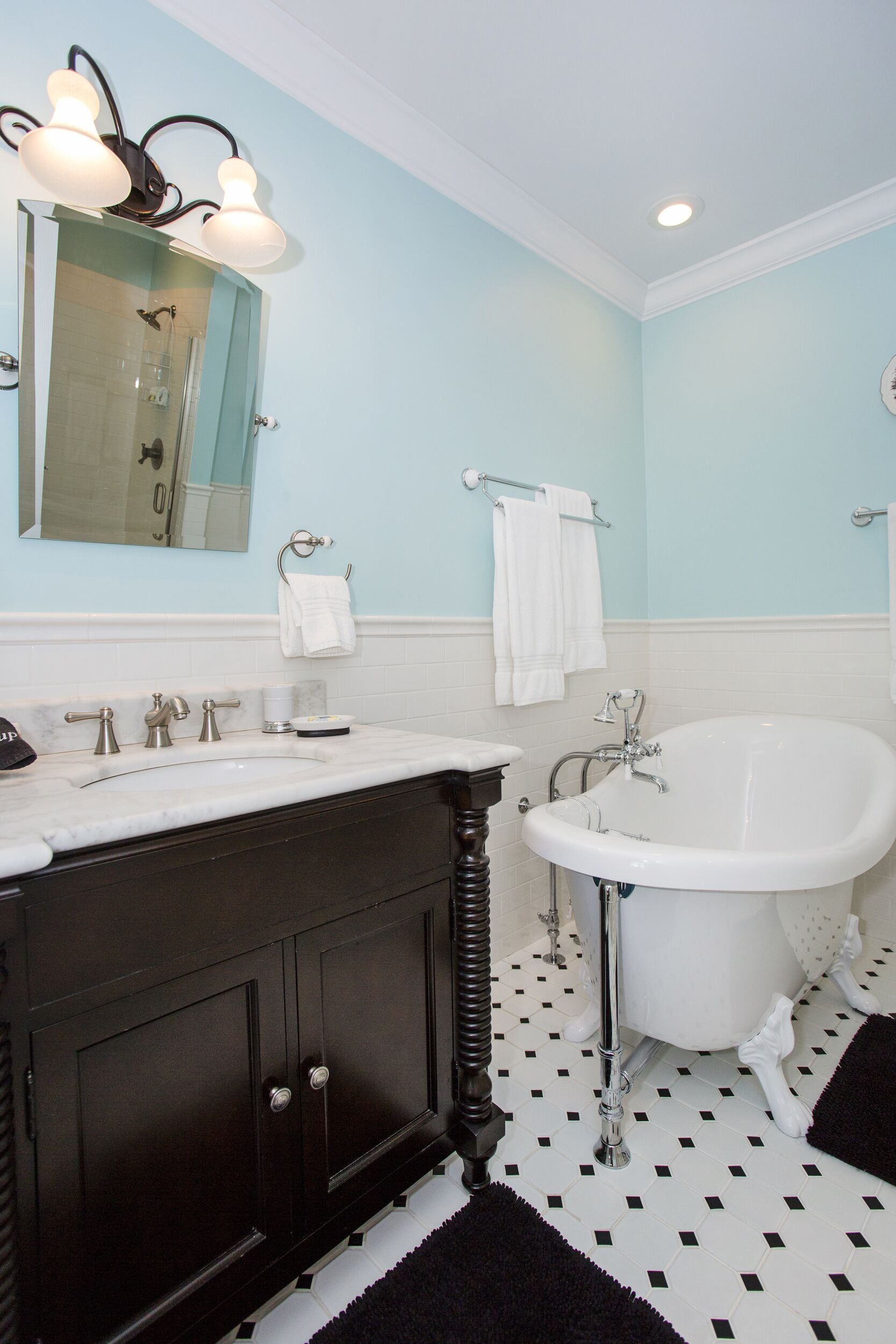 A bathroom with a white bathtub, dark wooden vanity, and a light blue wall.