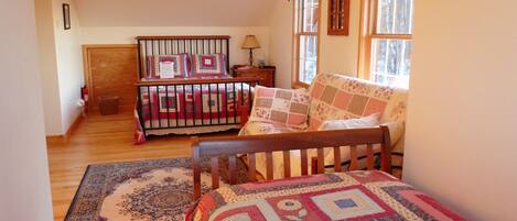 A cozy bedroom with a wooden bed, a matching bench, a patterned rug, and a window with curtains.