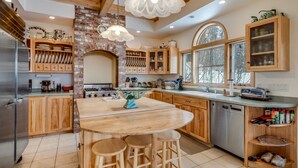A modern kitchen with wooden cabinets, a central island with stools, a brick wall, and a large window.