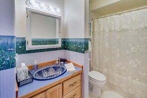A bathroom with a blue and white tiled vanity, a white toilet, and a shower curtain with floral patterns.