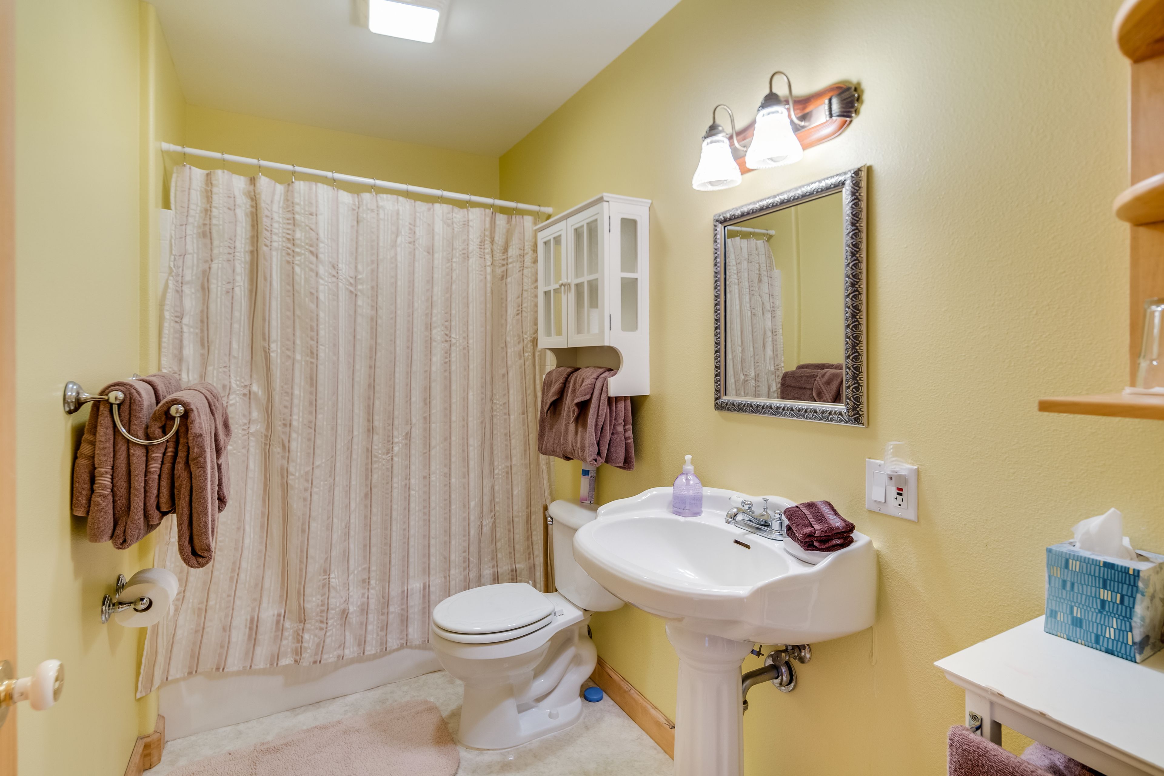 A bathroom with a toilet, sink, and shower curtain. There are towels hanging on the wall and a mirror above the sink.