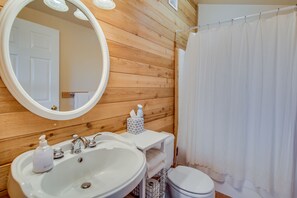 A bathroom with a wooden wall, a white sink, a mirror, a toilet, and a shower curtain.