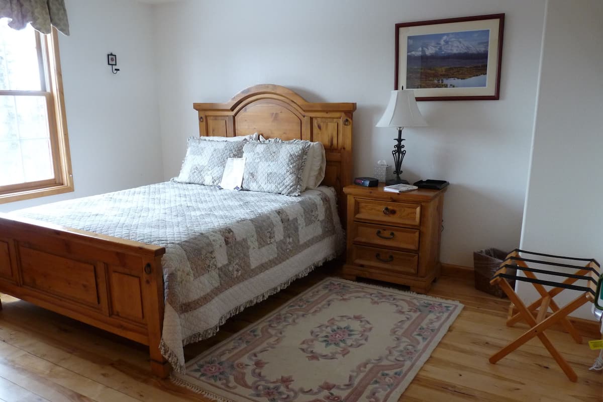 Quarto com cama de madeira, mesa de cabeceira, abajur, quadro na parede e luminária de chão.
