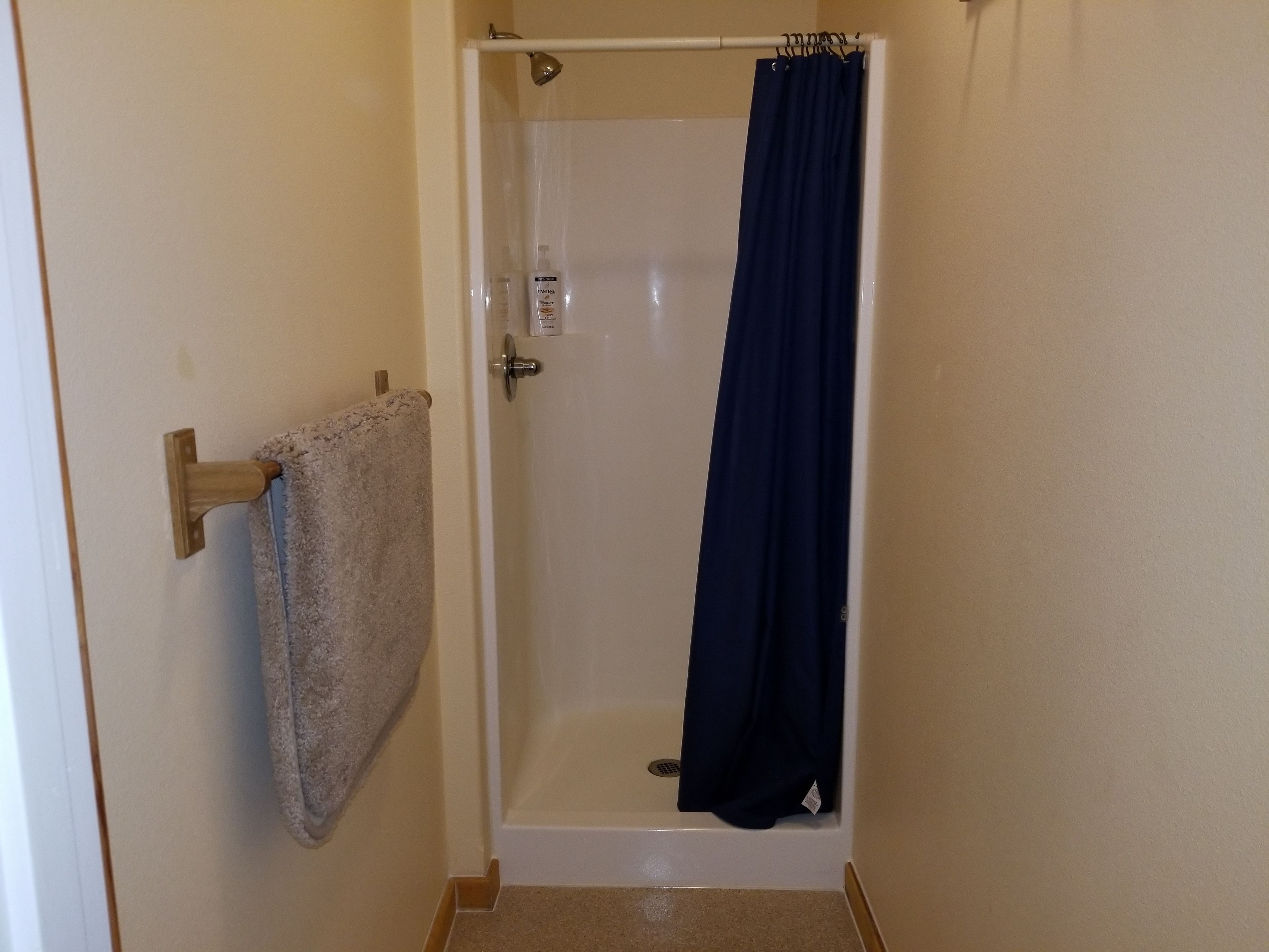 Un petit espace douche fermé, avec une porte blanche, un porte-serviettes avec une serviette et un rideau de douche foncé.