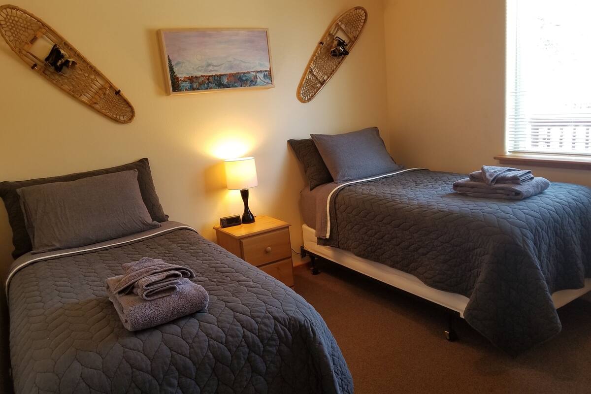 A bedroom with two beds, a nightstand with a lamp, and a painting on the wall.