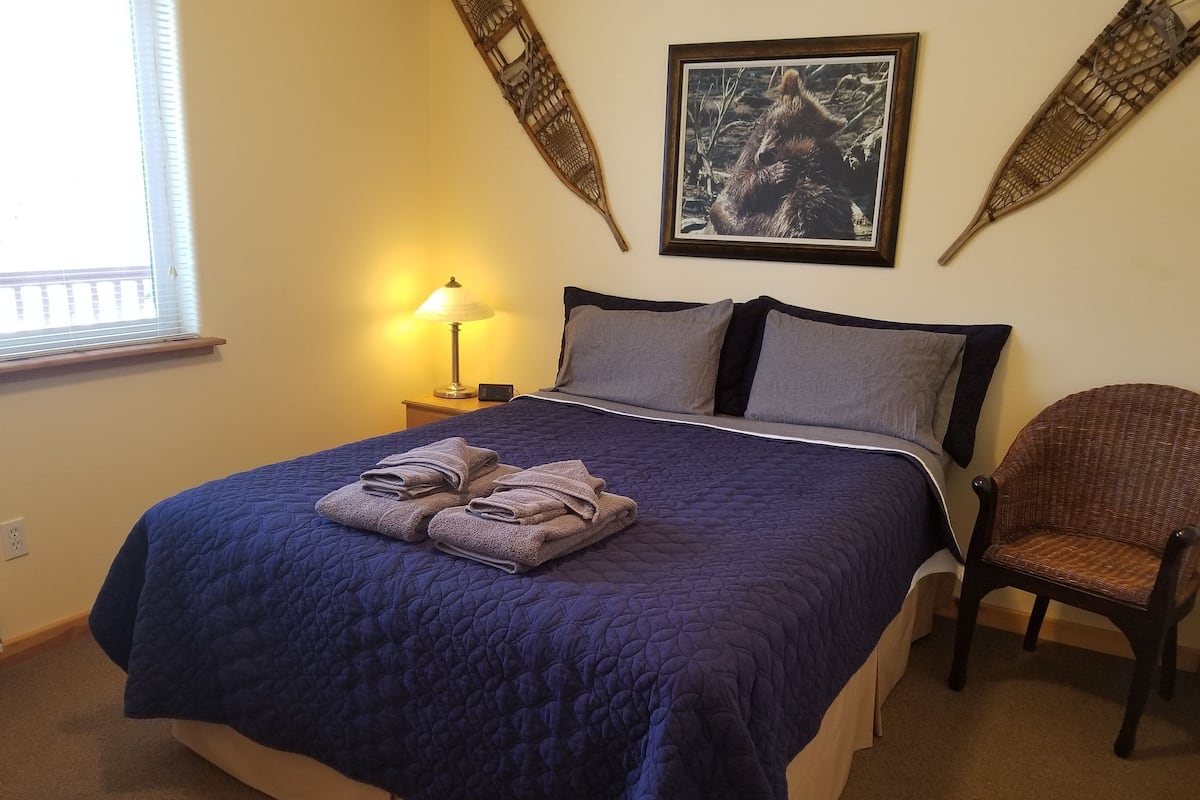 A bedroom with a large bed, a chair, a lamp, and a framed picture on the wall.