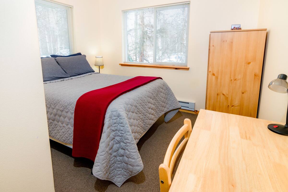 A bedroom with a bed, a desk, and a wardrobe.