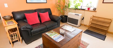 Un salon avec un canapé en cuir noir, une table basse en bois sur laquelle sont posés des magazines, une plante en pot et une carte accrochée au mur.