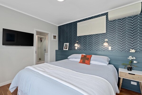 A bedroom with a bed, bedside table, wall-mounted TV, and patterned wallpaper. - Devonport Motel (Auckland)