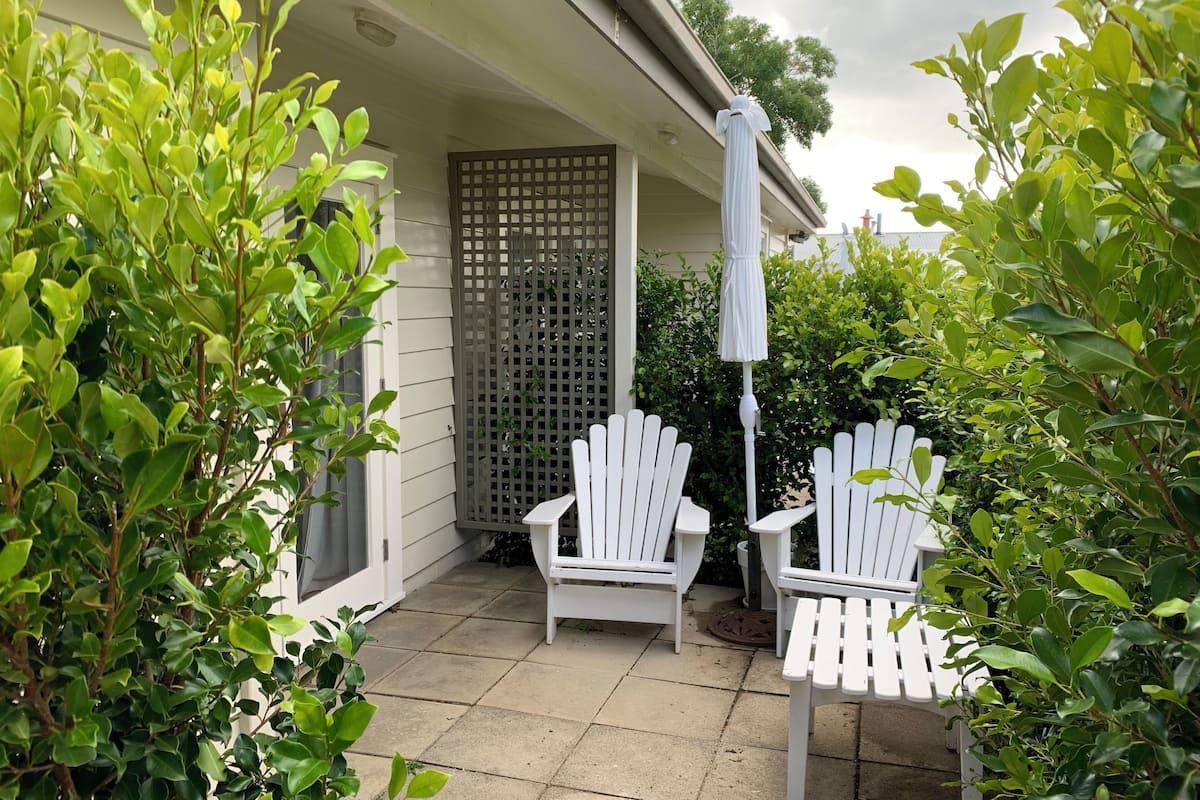 A patio with two white Adirondack chairs, a white umbrella, and a lattice screen.