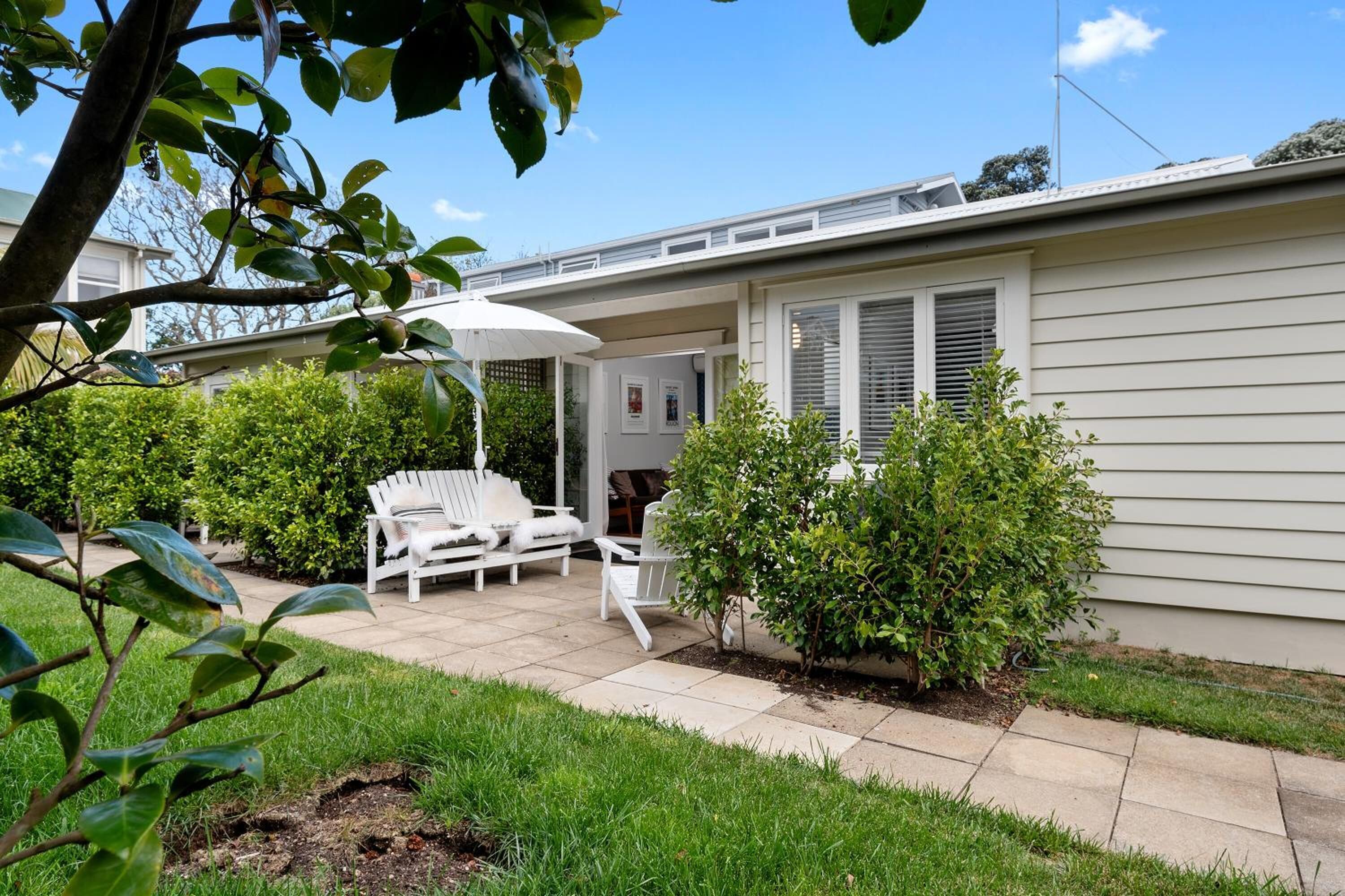A patio area with a white outdoor chair and table, surrounded by greenery and a small bush.
