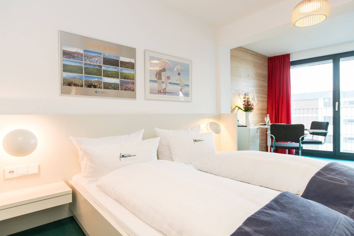 A hotel room with a large bed, a desk with a chair, and a view of the city through the window.