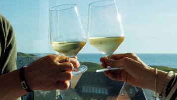 Two hands holding wine glasses with a coastal view in the background.