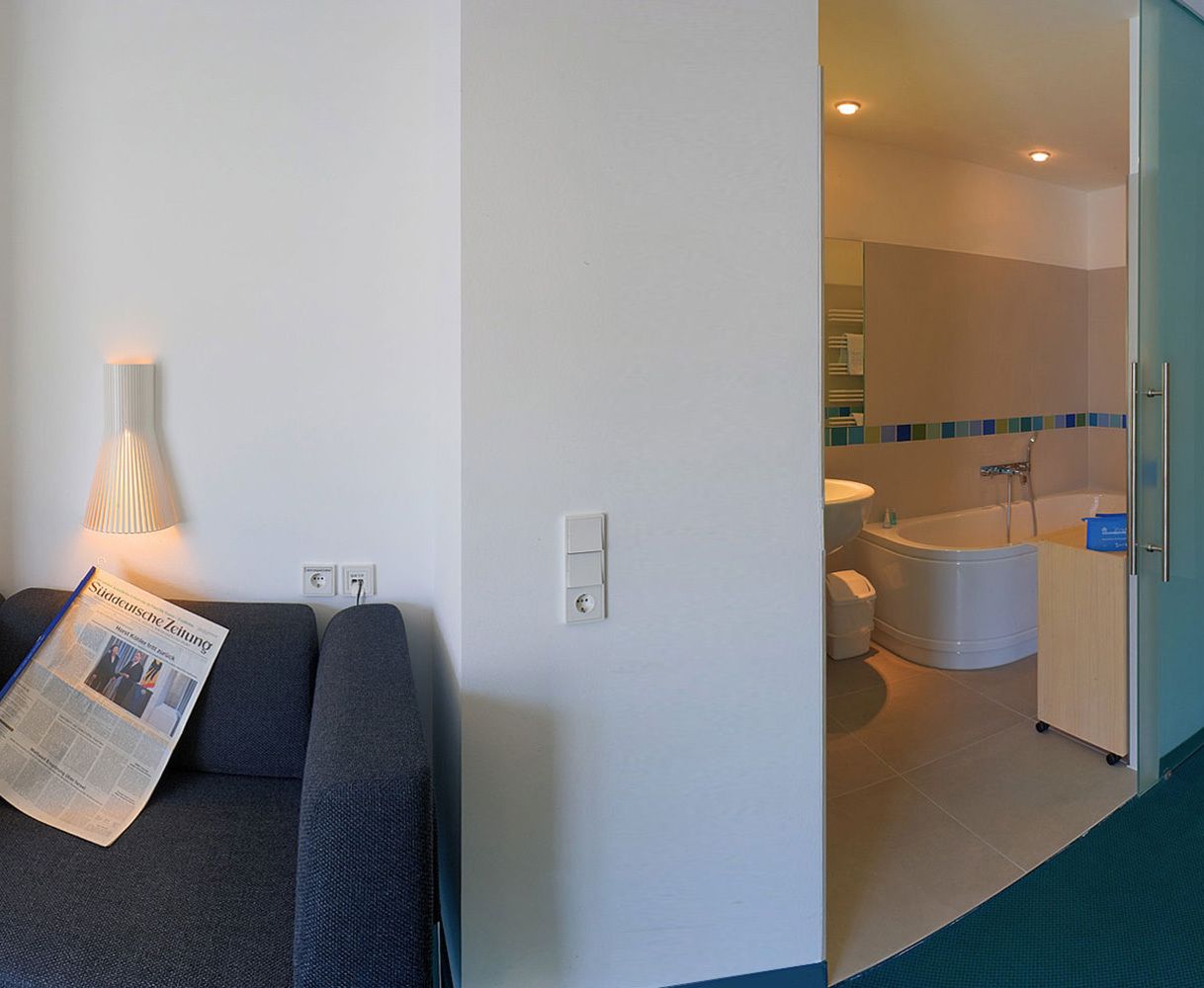 Habitación de hotel con sofá, lámpara, periódico, baño con bañera y retrete.