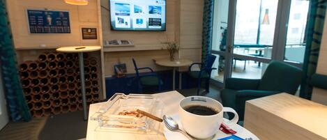 A hotel reception area with a coffee table, a cup of coffee, a cigar, and a menu board.