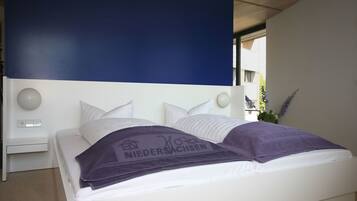 Een moderne slaapkamer met een wit bed, een blauwe accentmuur en uitzicht op de omgeving.