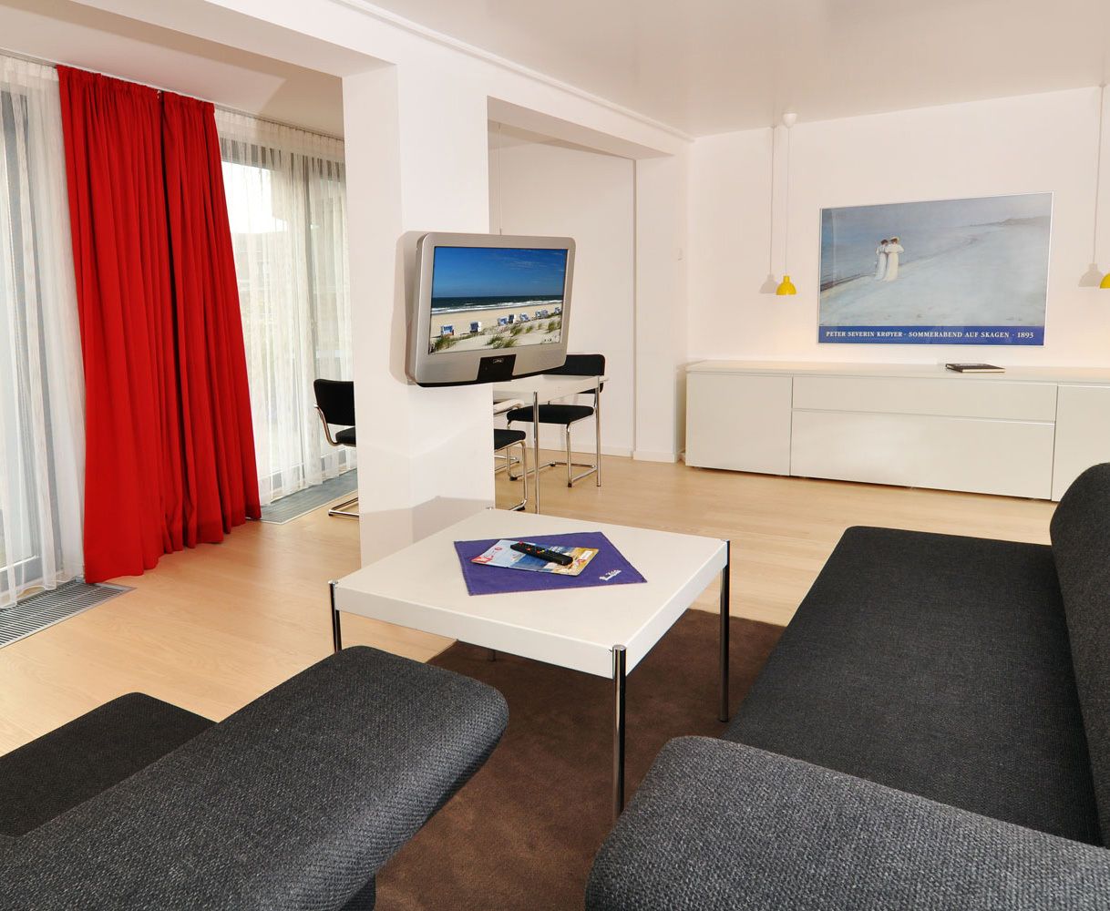 Een moderne woonkamer met een flatscreen televisie, een klein tafeltje en grijze banken.