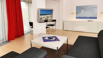 Een moderne woonkamer met een flatscreen televisie, een klein tafeltje en grijze banken.