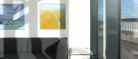 A modern interior with a sofa, artwork, and a view of the deck.