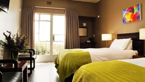 A hotel room with two beds, a desk, chairs, a TV, and a window with curtains.