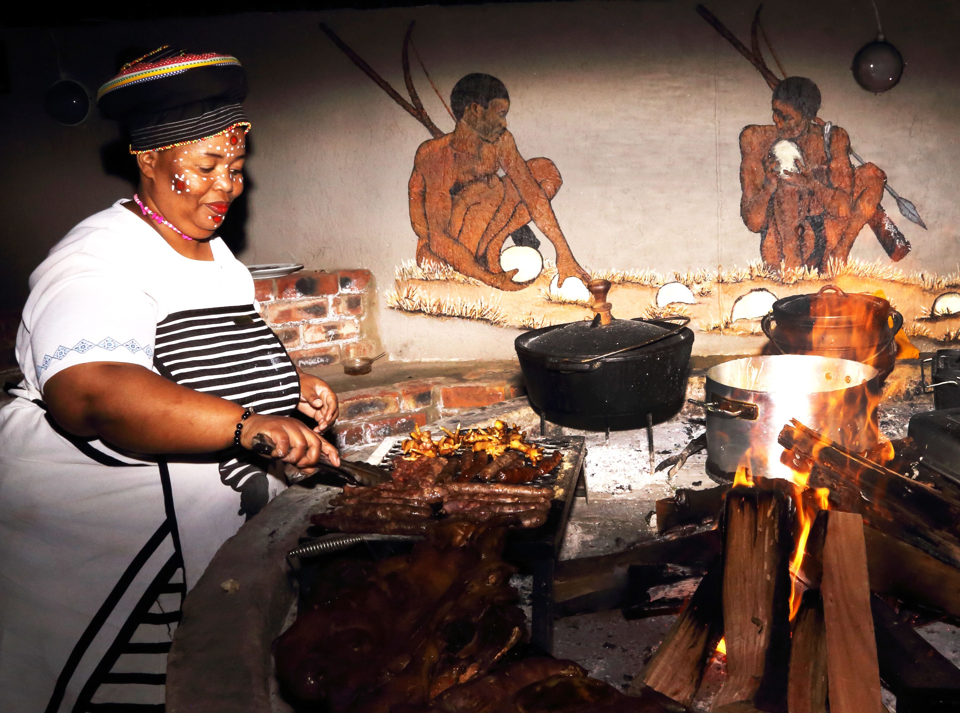 A person cooking outdoors with a fire, a pot, and a grill.