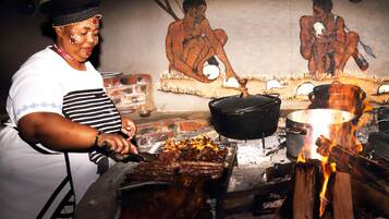 A person cooking outdoors with a fire, a pot, and a grill.
