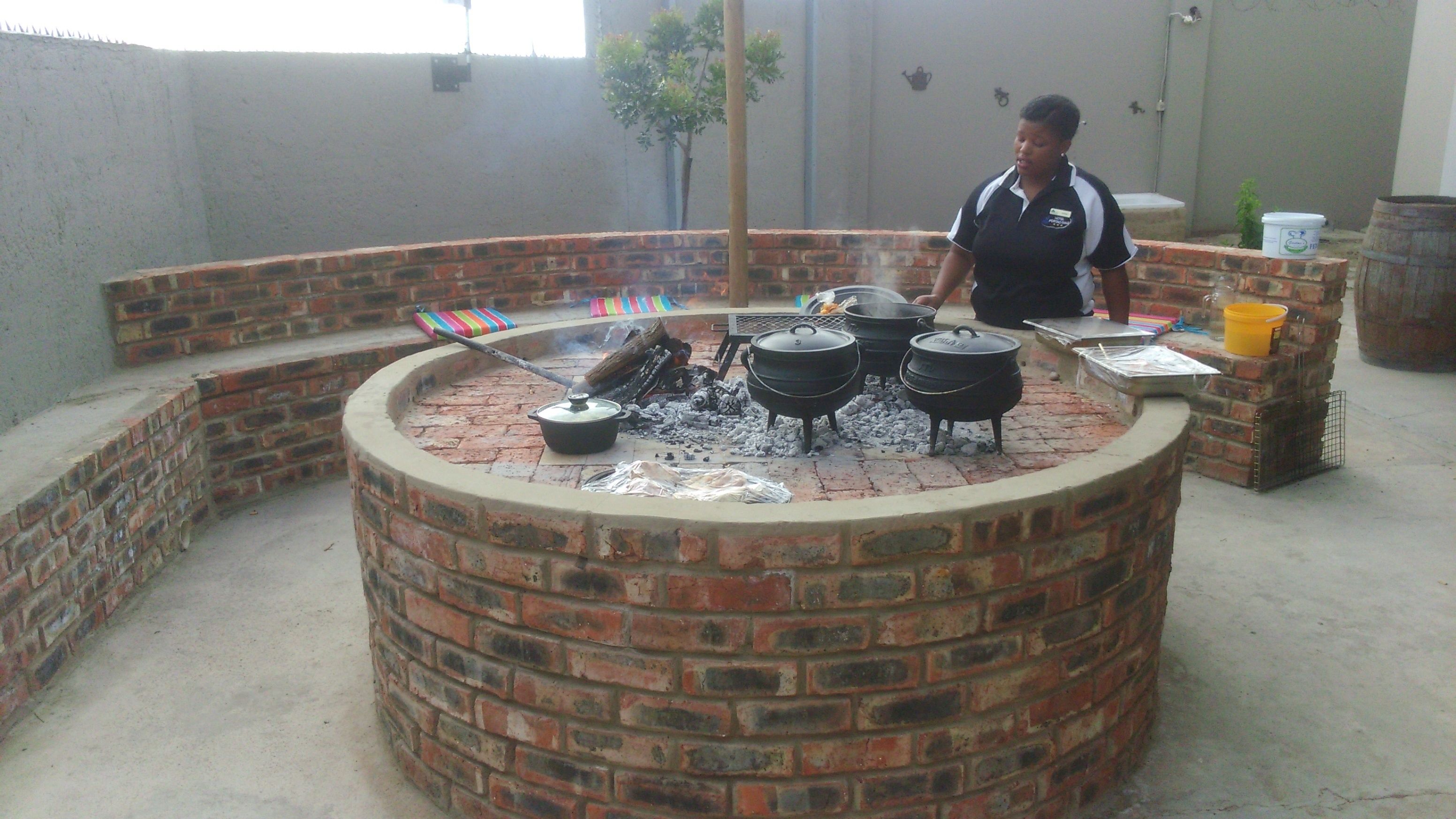 A circular brick barbecue pit with cooking pots and a grill.
