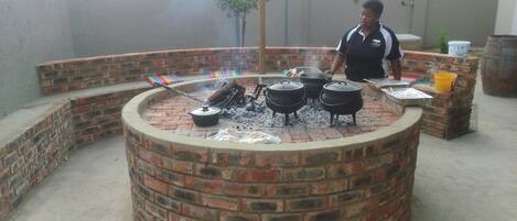 A circular brick barbecue pit with cooking pots and a grill.