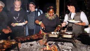 A group of people around a barbecue grill with food being cooked.