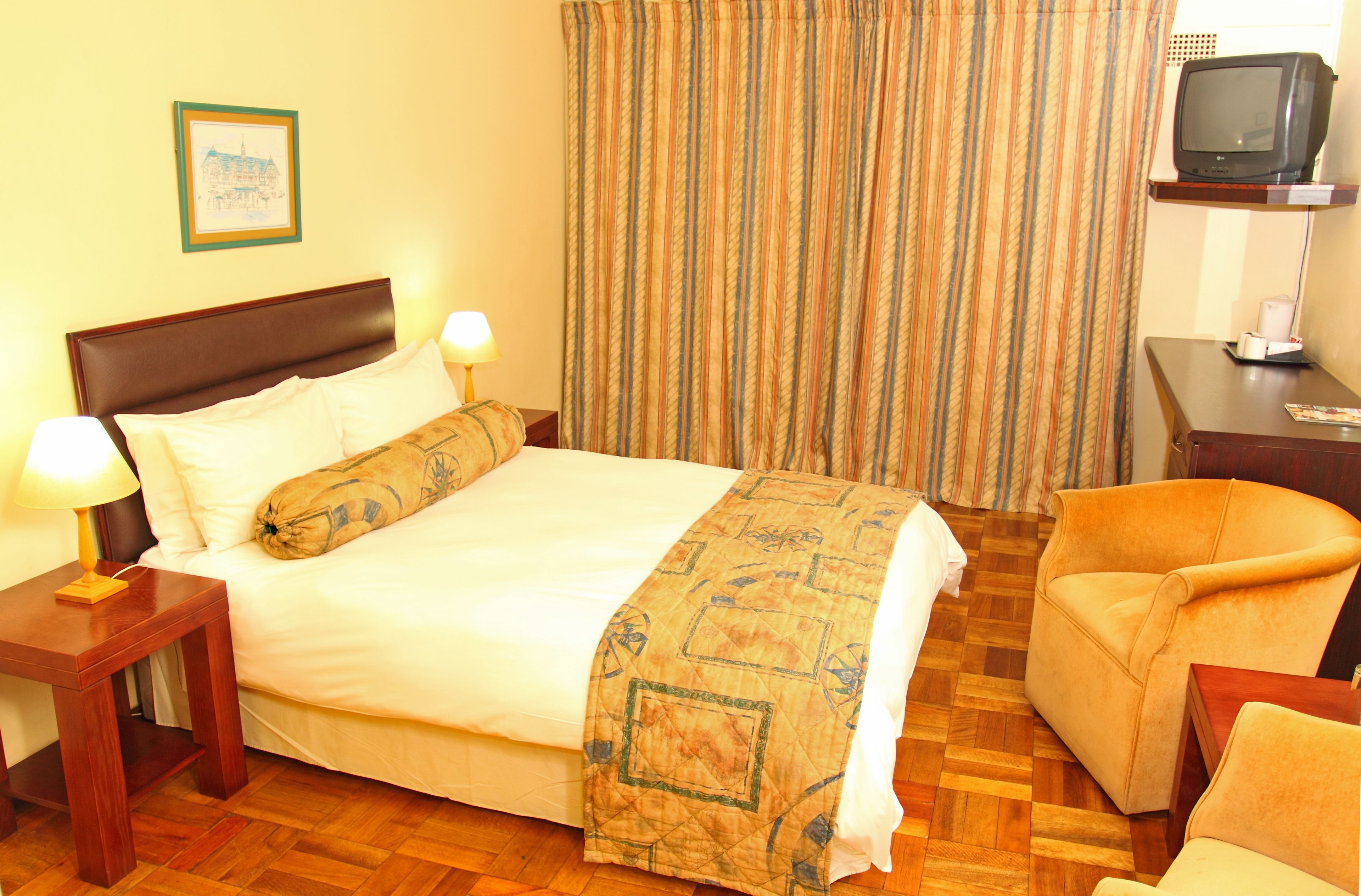 A hotel room with a bed, a chair, a TV, and a nightstand with a lamp.