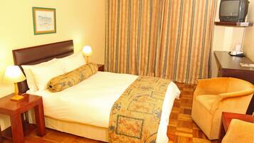 A hotel room with a bed, a chair, a TV, and a nightstand with a lamp.